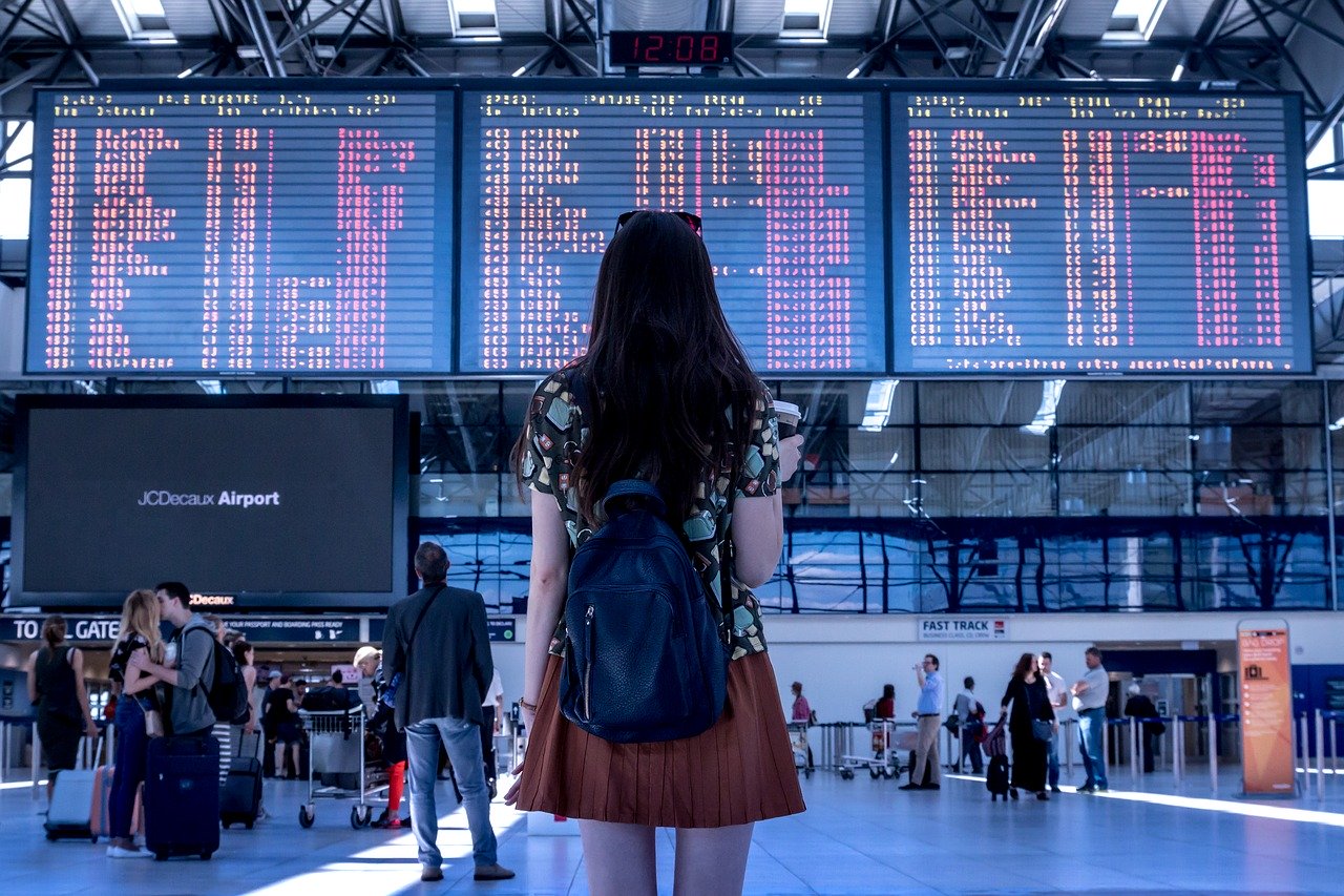 junge Frau vor Flughafen Abflugtafel